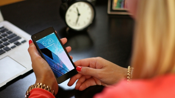 woman holding cell phone sitting at work desk with clock